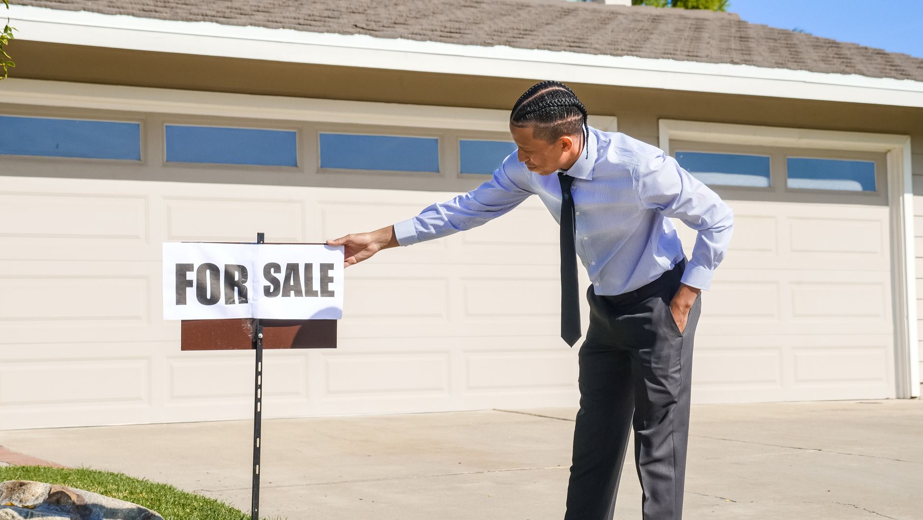 Professional real estate agent setting up a for sale sign outside a house.