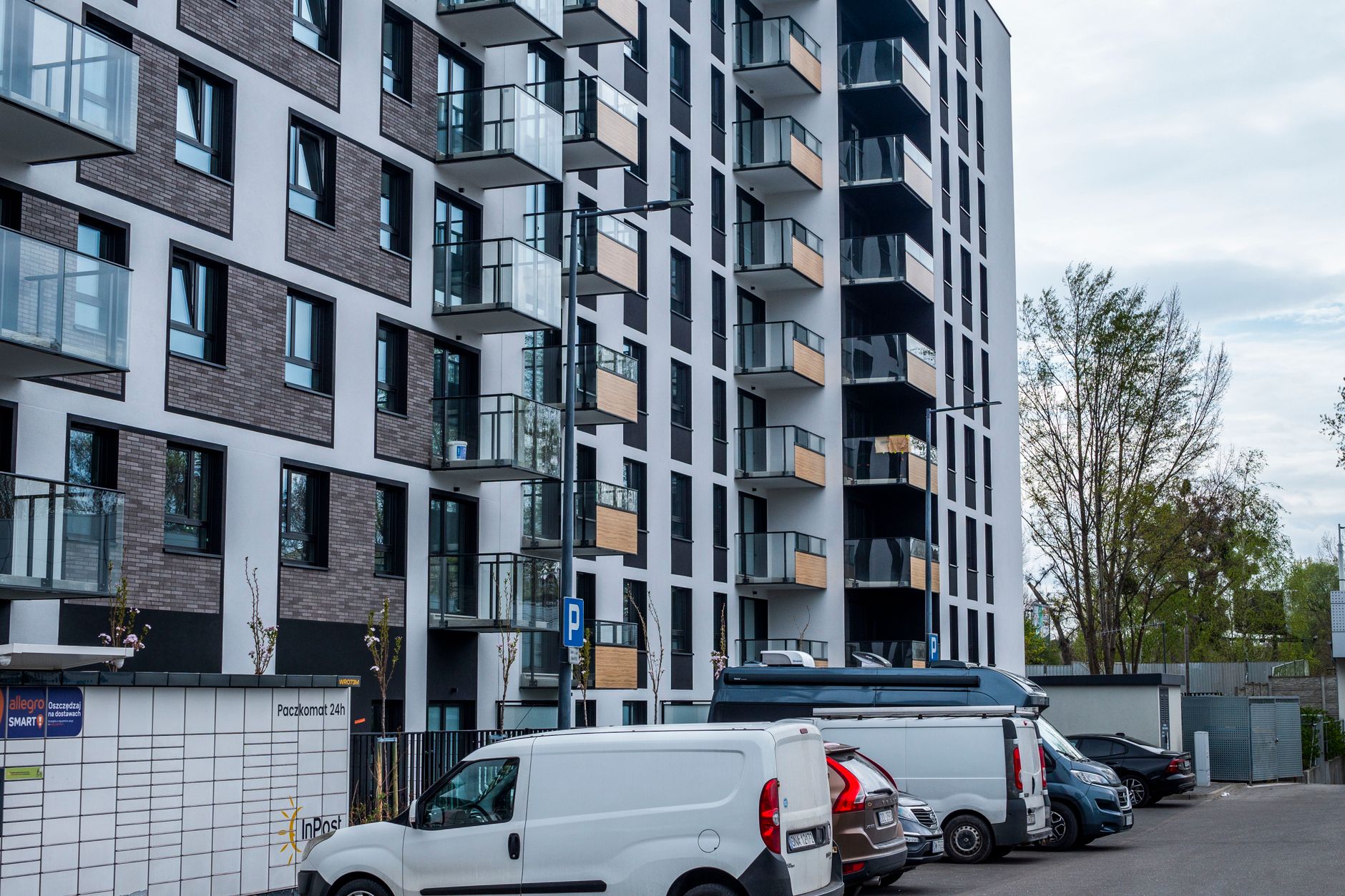 Contemporary apartment building with parking area and vehicles in a city setting.