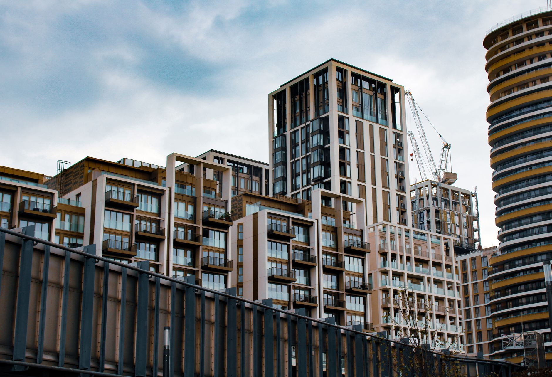A low angle view of modern apartment buildings and cranes under an overcast sky in the city.