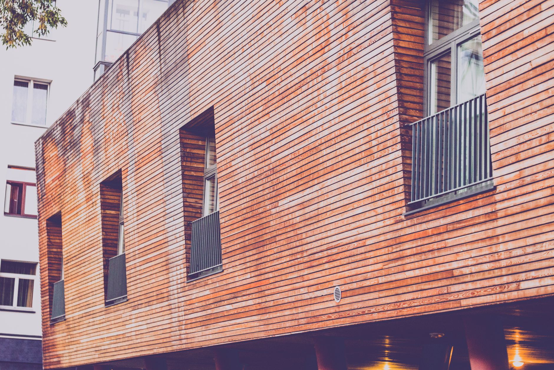 Contemporary wooden facade of a residential building with windows and railings, showcasing urban architecture.