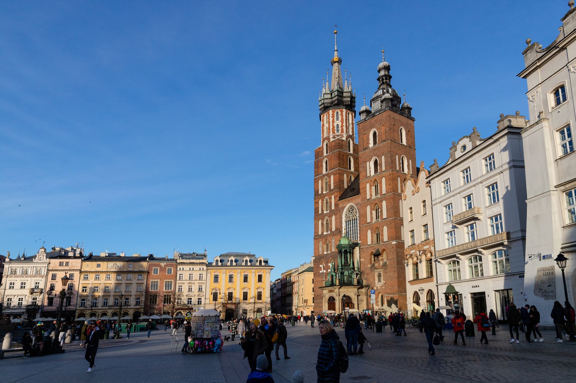 Daytime view of St. Mary's Basilica in Krakow's Main Market Square, under clear blue skies.