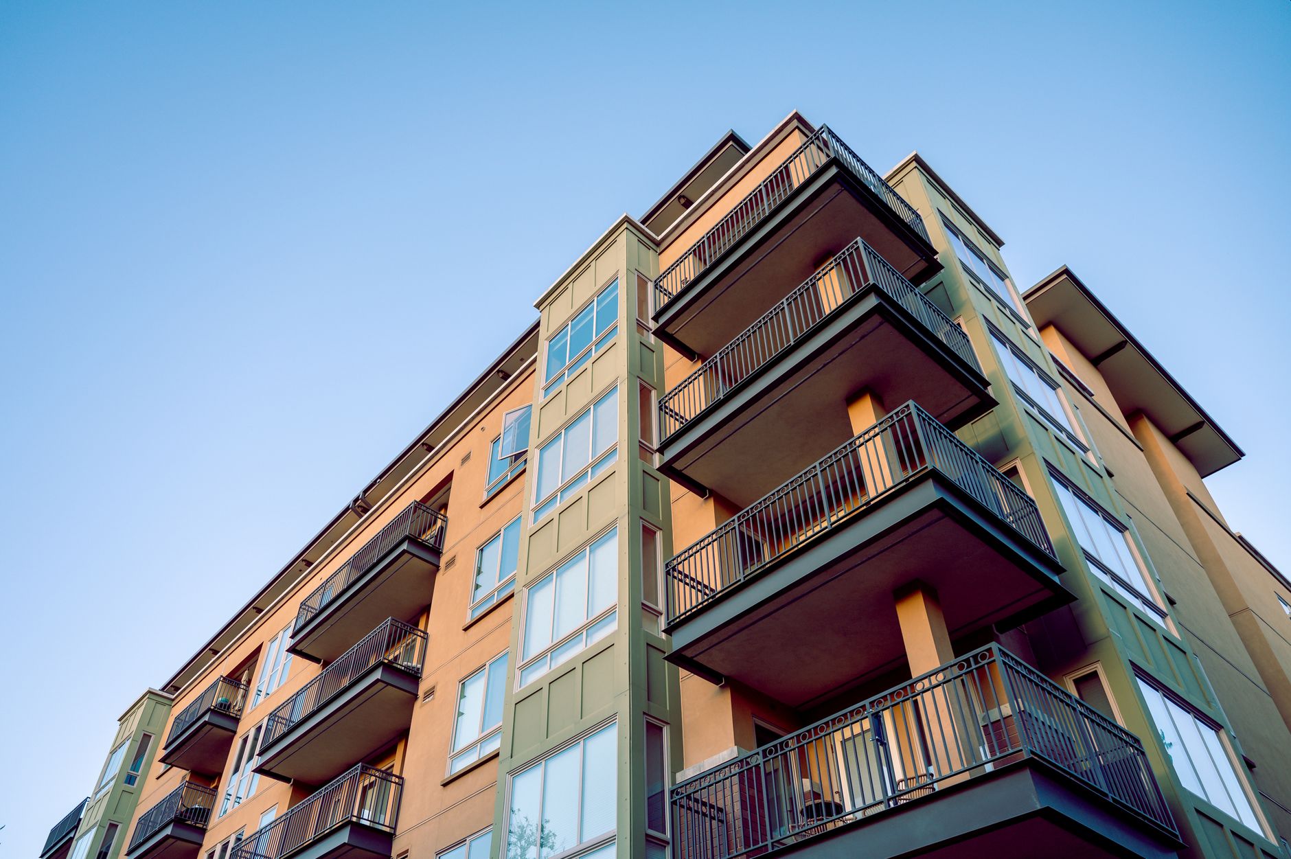 Contemporary city apartment building with multiple balconies and glass windows.