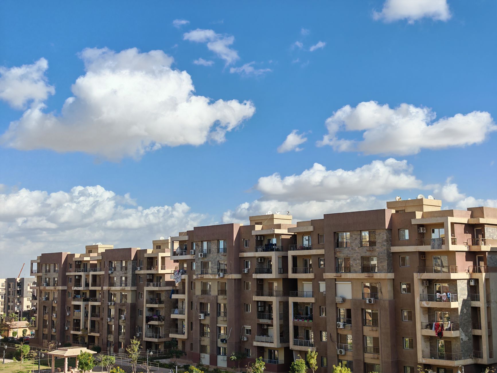 Spacious modern apartment buildings under a bright blue sky with fluffy clouds.