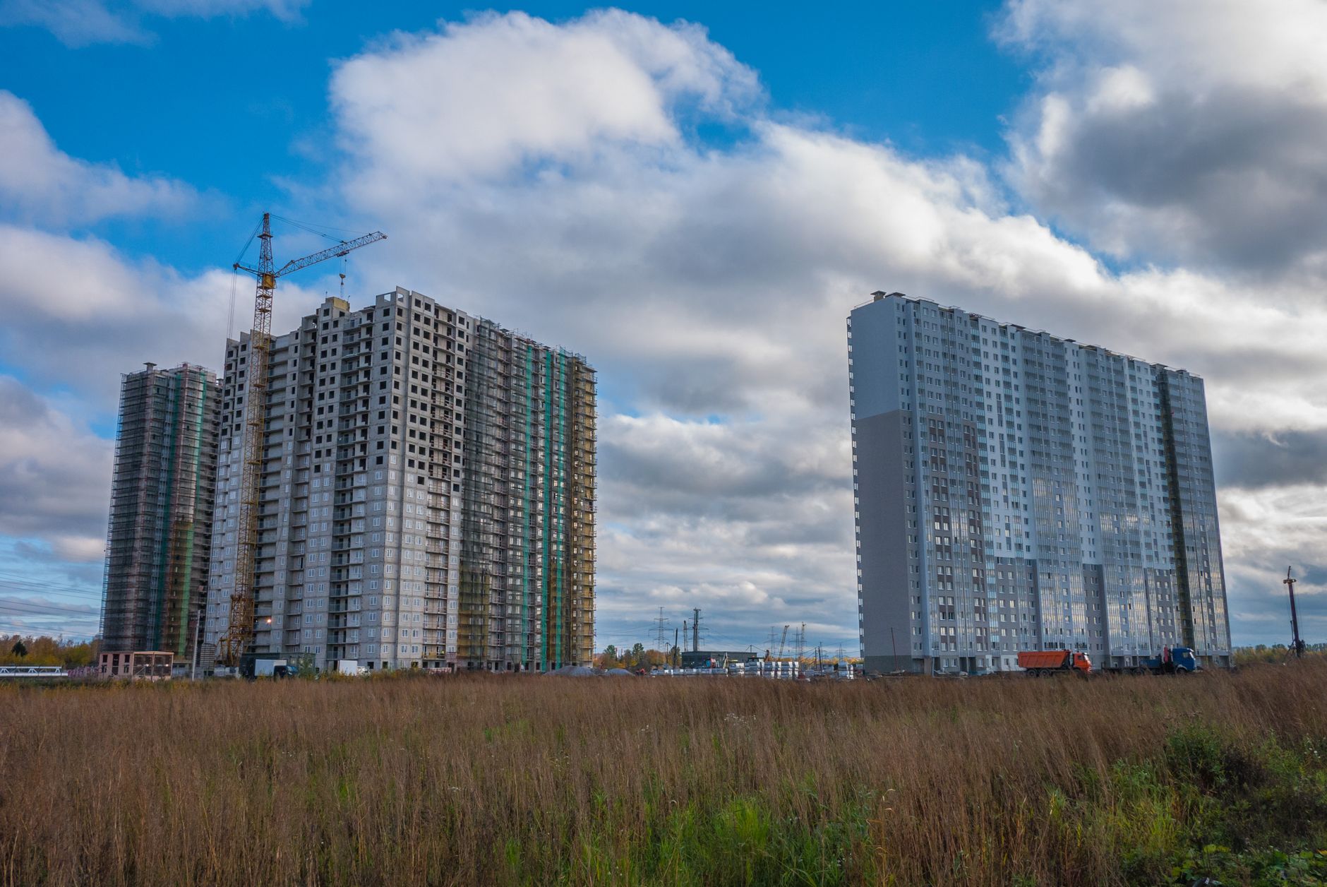 Two high-rise buildings under construction with cranes against a blue sky.
