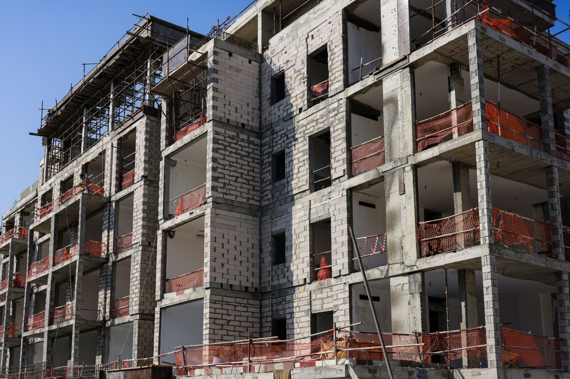 A modern multi-story apartment building under construction with scaffolding and safety netting.