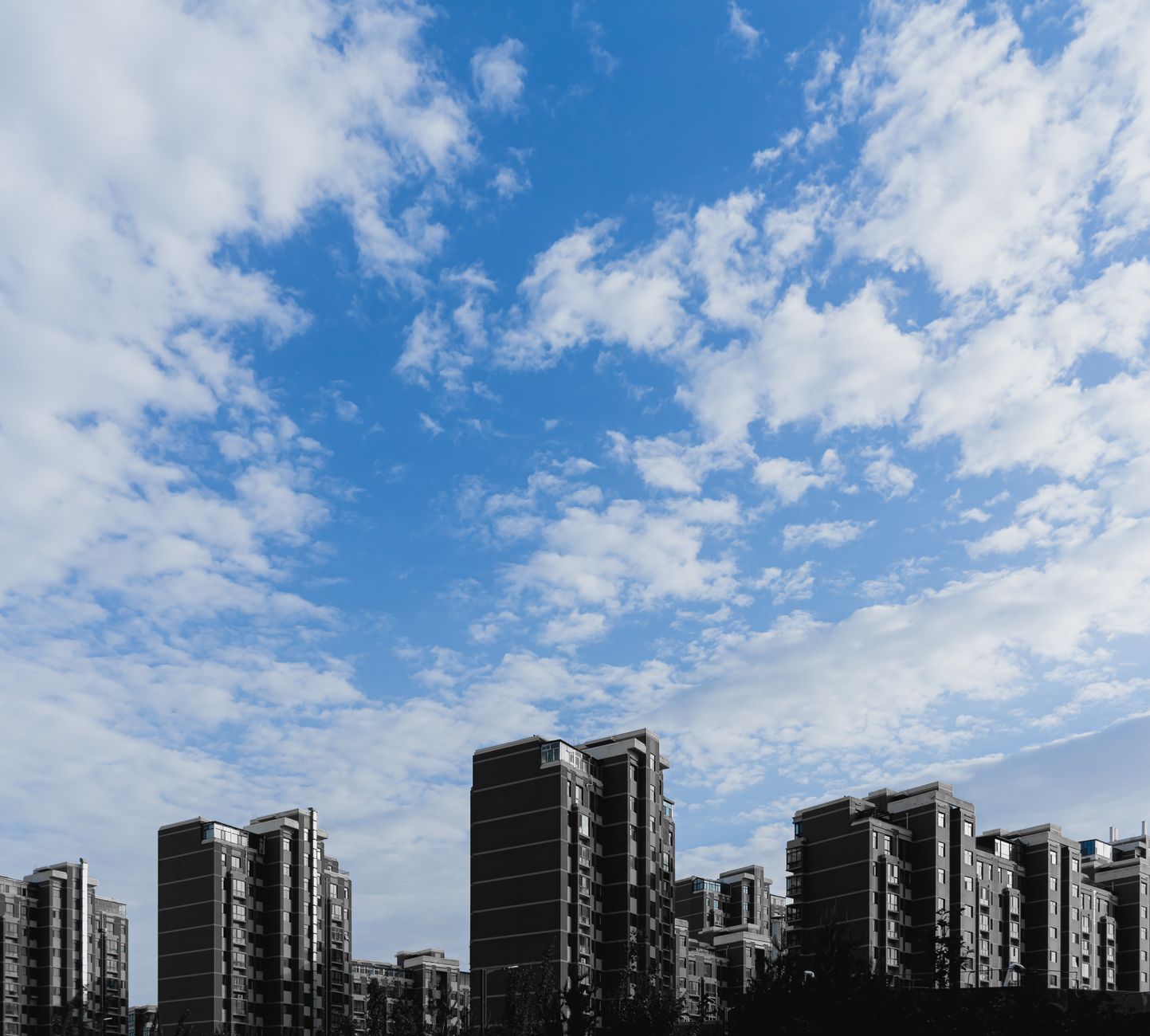 Contemporary high-rise apartments against a bright and cloudy sky, showcasing urban architecture.