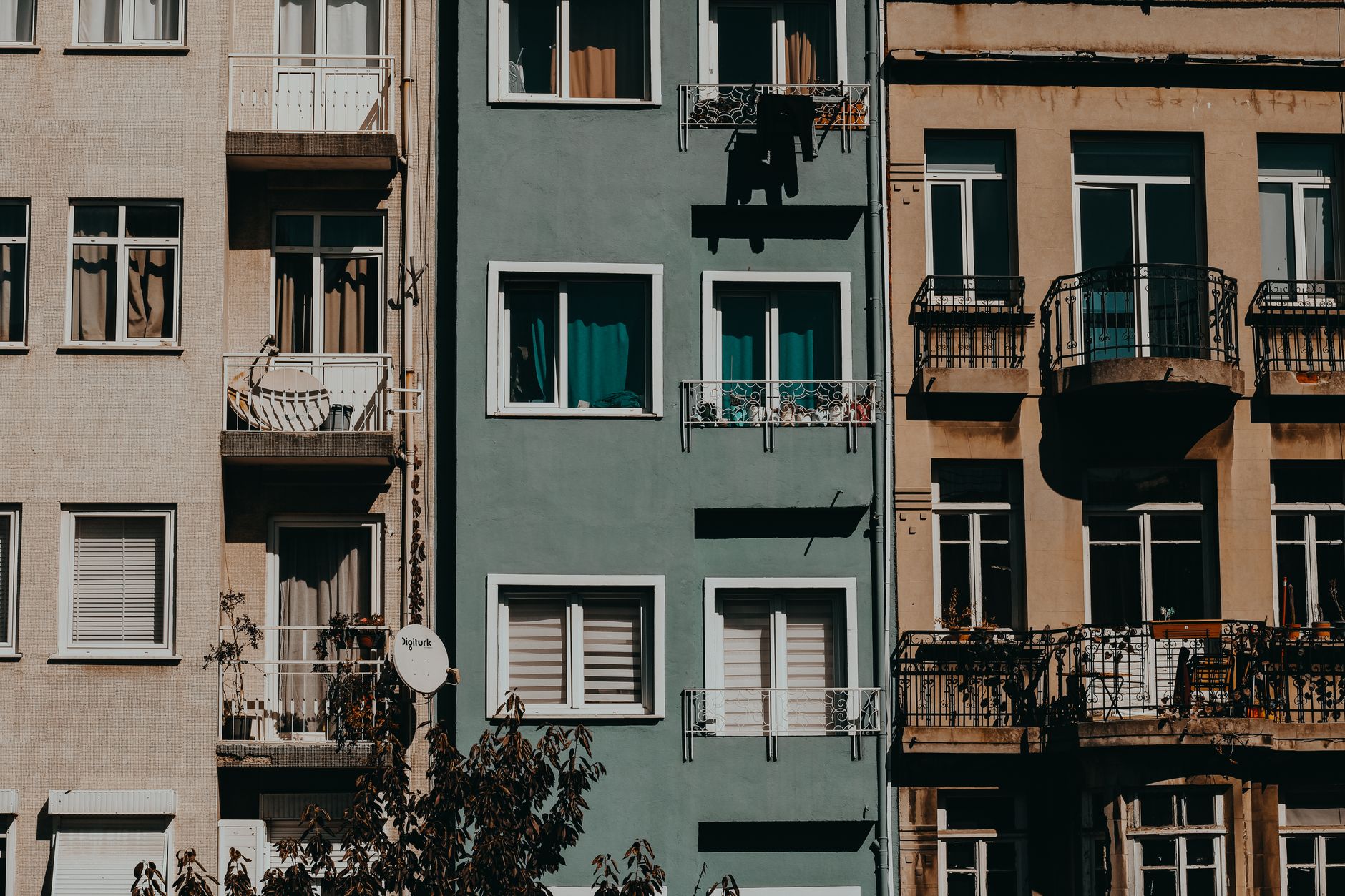 A row of urban apartment buildings with balconies and varied facades basking in sunlight, showcasing city architecture.