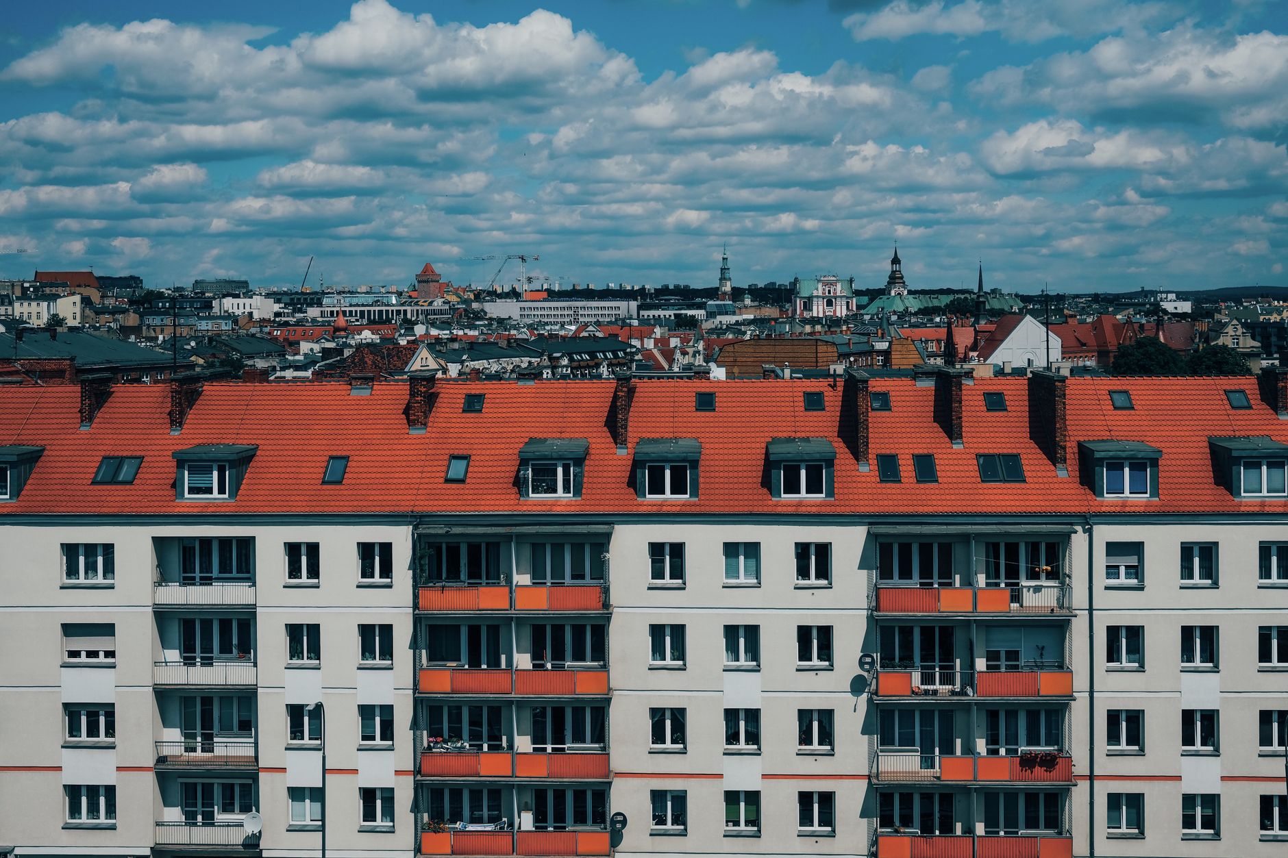 A picturesque view of Poznań's urban landscape featuring red-roofed buildings and the downtown skyline under a cloudy sky.