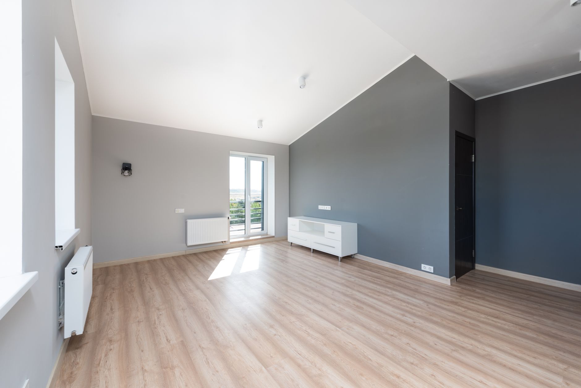 Wide-angle shot of a modern unfurnished apartment with wooden flooring and large windows.