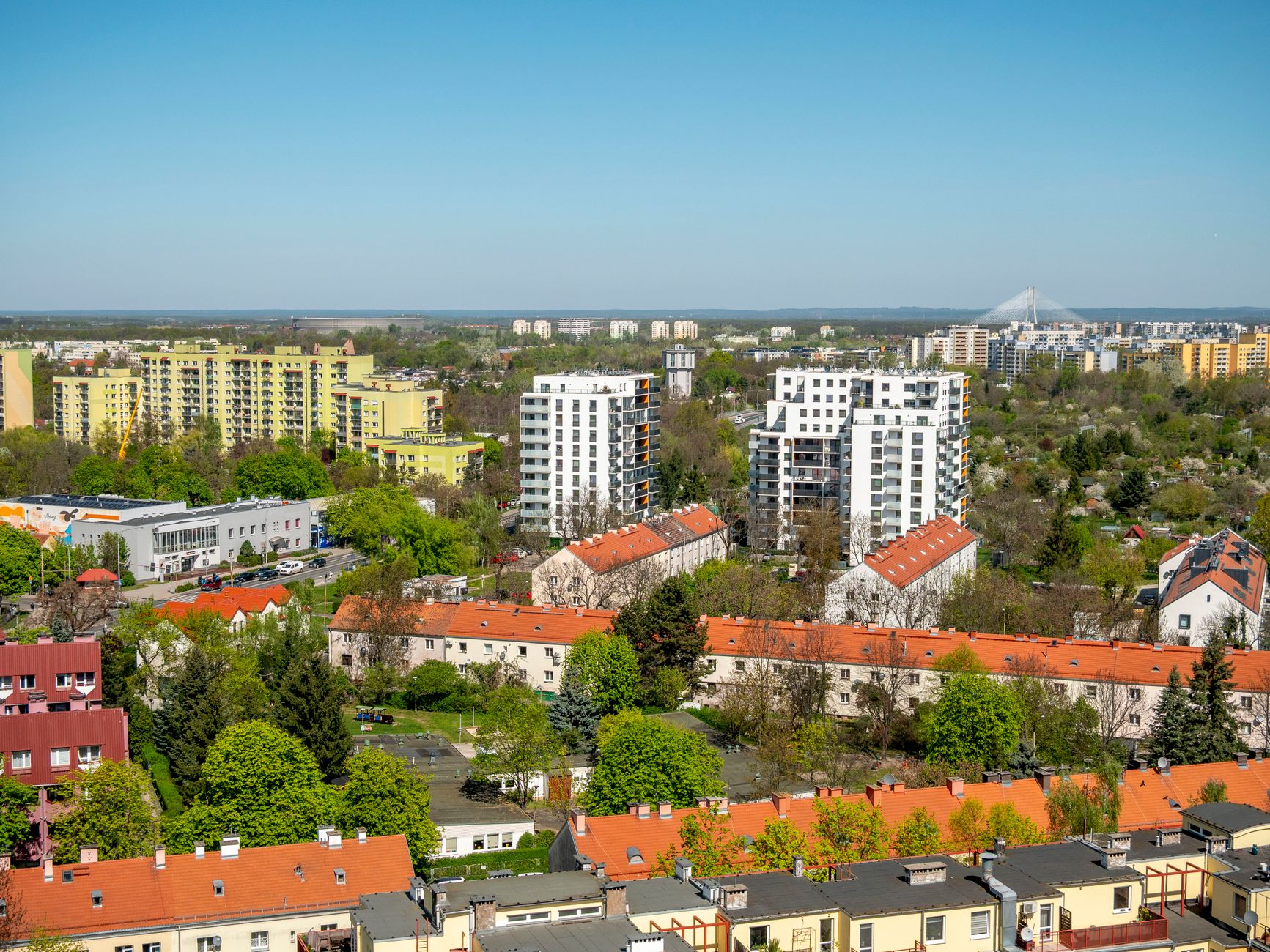 Aerial view of Wrocław showcasing residential buildings and green landscapes under a clear sky.
