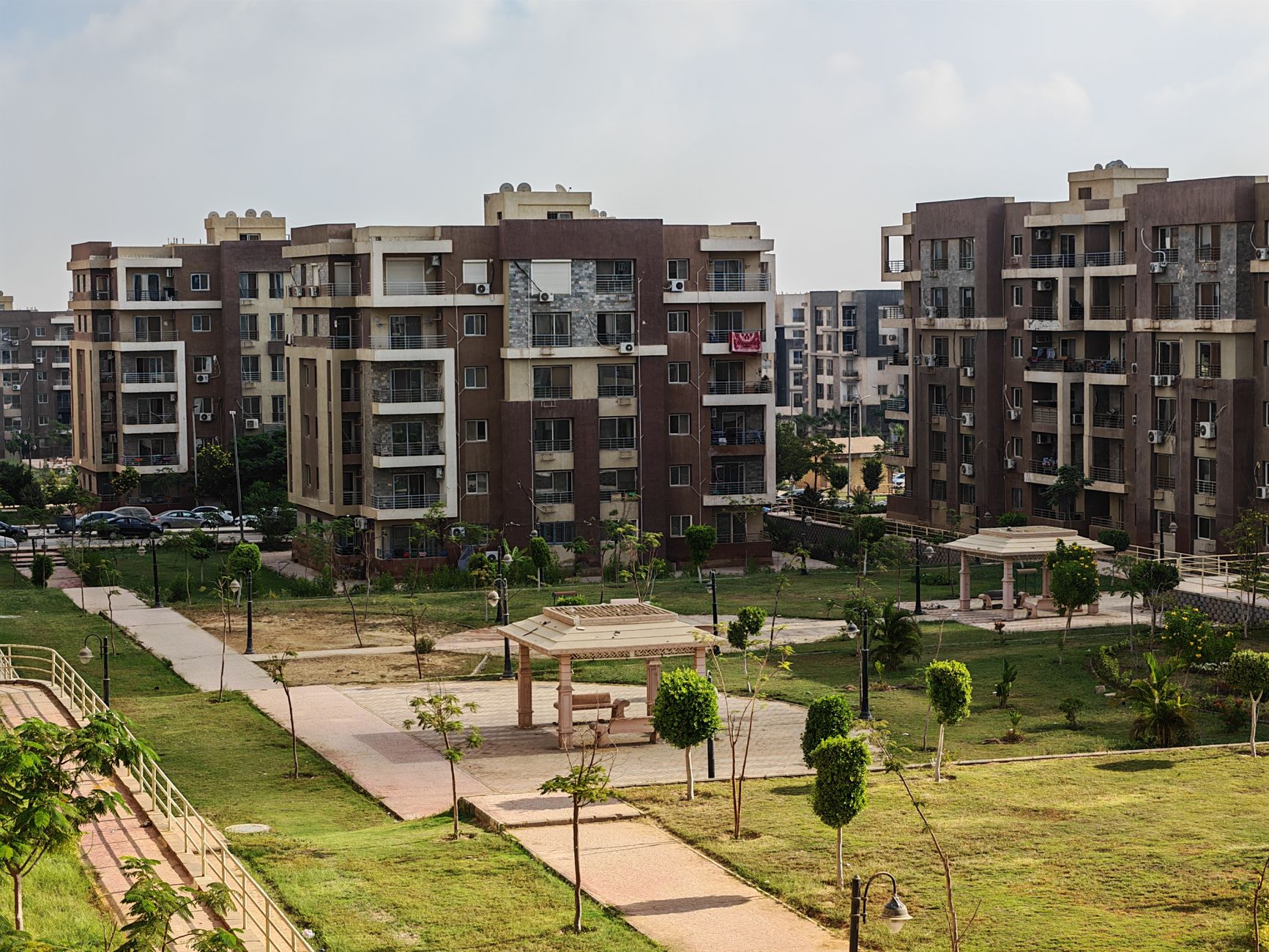A modern apartment complex featuring green urban park with pathways and recreational structures.