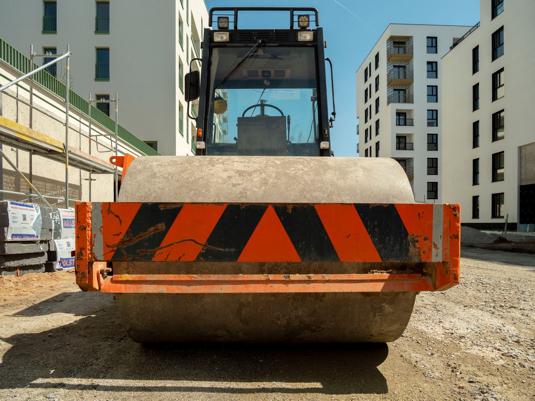 Close-up of a steamroller on a construction site in Wrocław, Poland with modern buildings in the background.