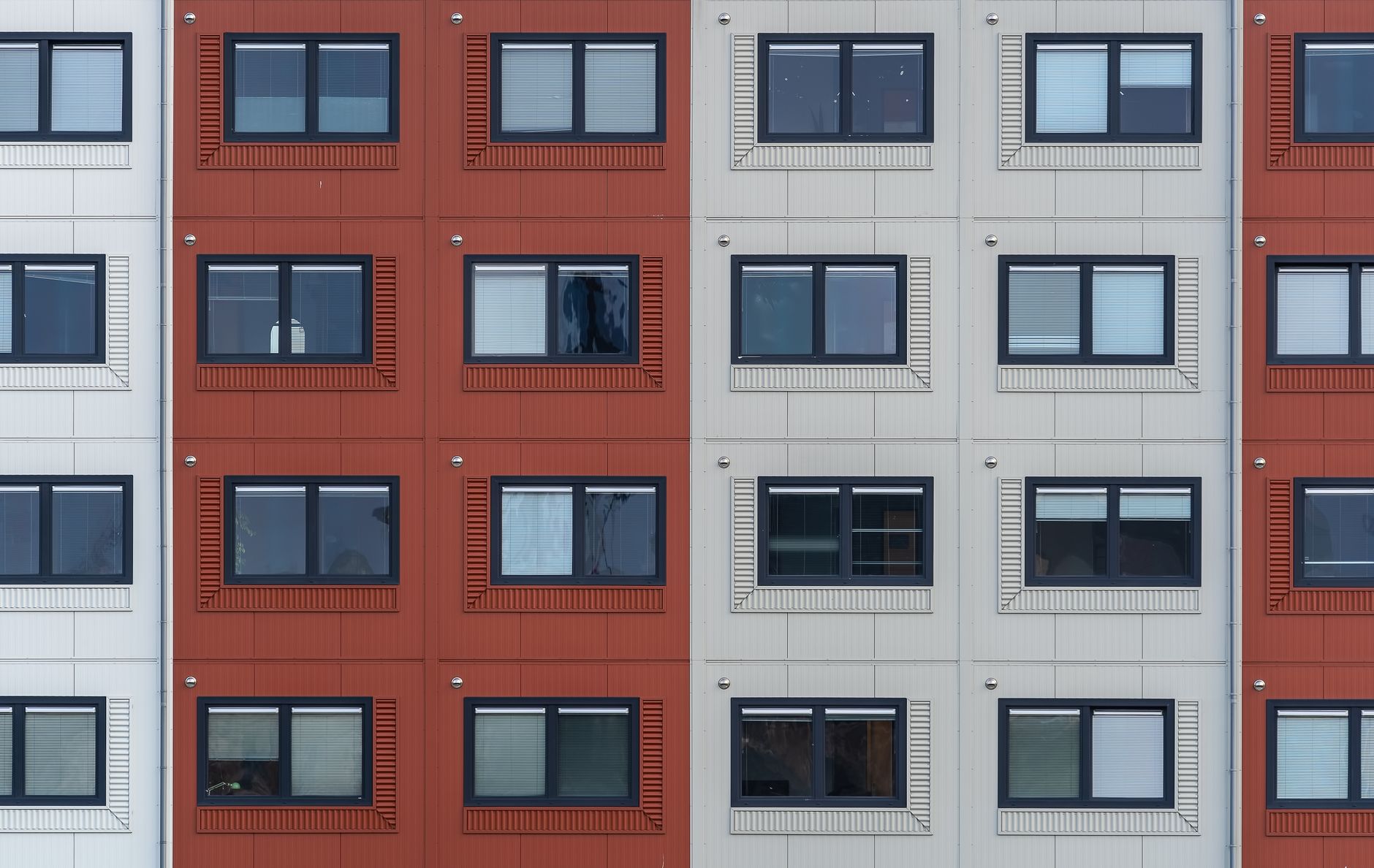 A modern residential building facade with repeating windows and geometric symmetry in red and white.