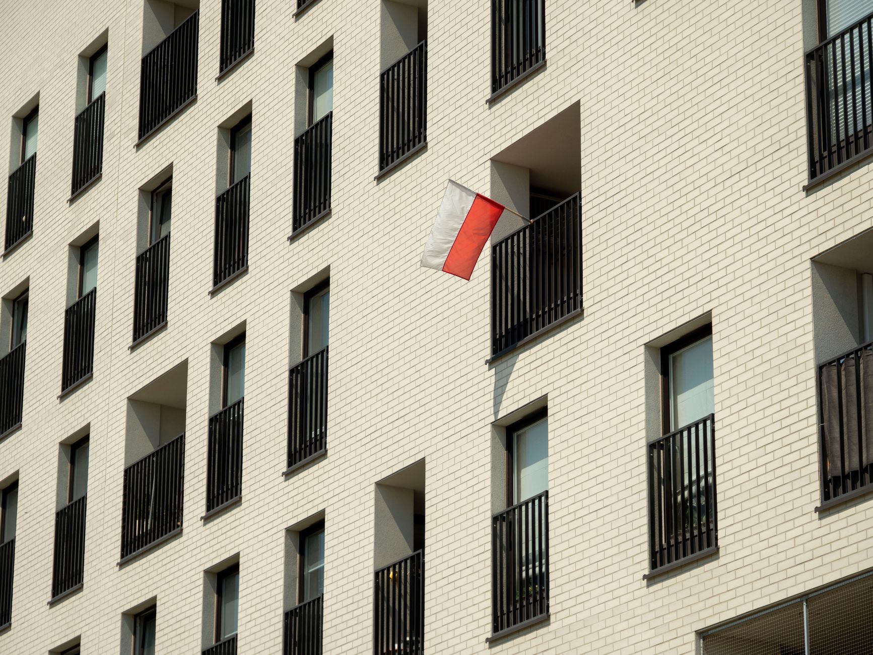 Angled view of a modern building in Wrocław, featuring a Polish flag on the balcony, showcasing urban architecture.