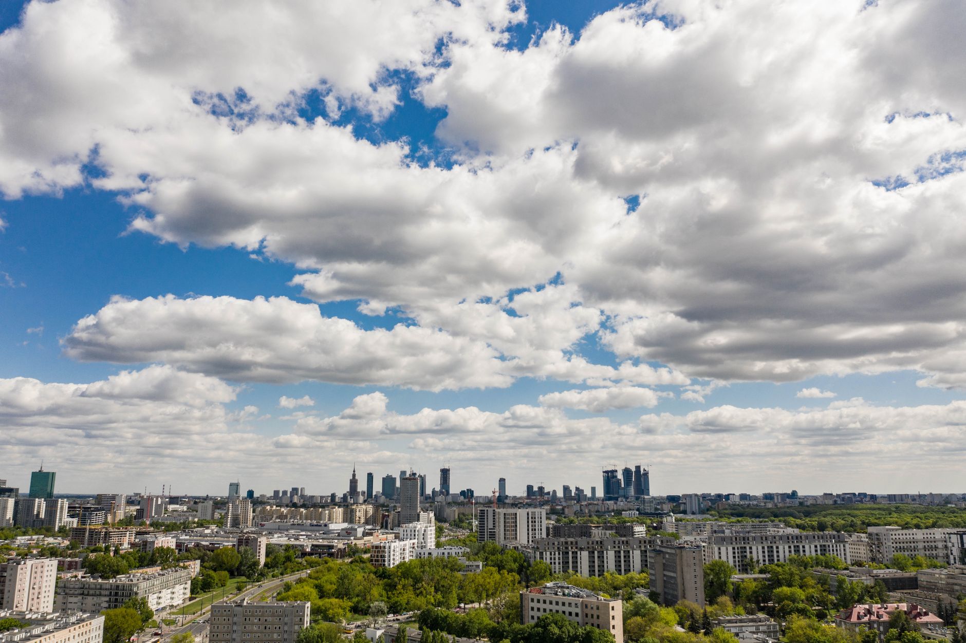 Stunning aerial view of Warsaw's cityscape with expansive clouds, showcasing urban architecture and greenery.
