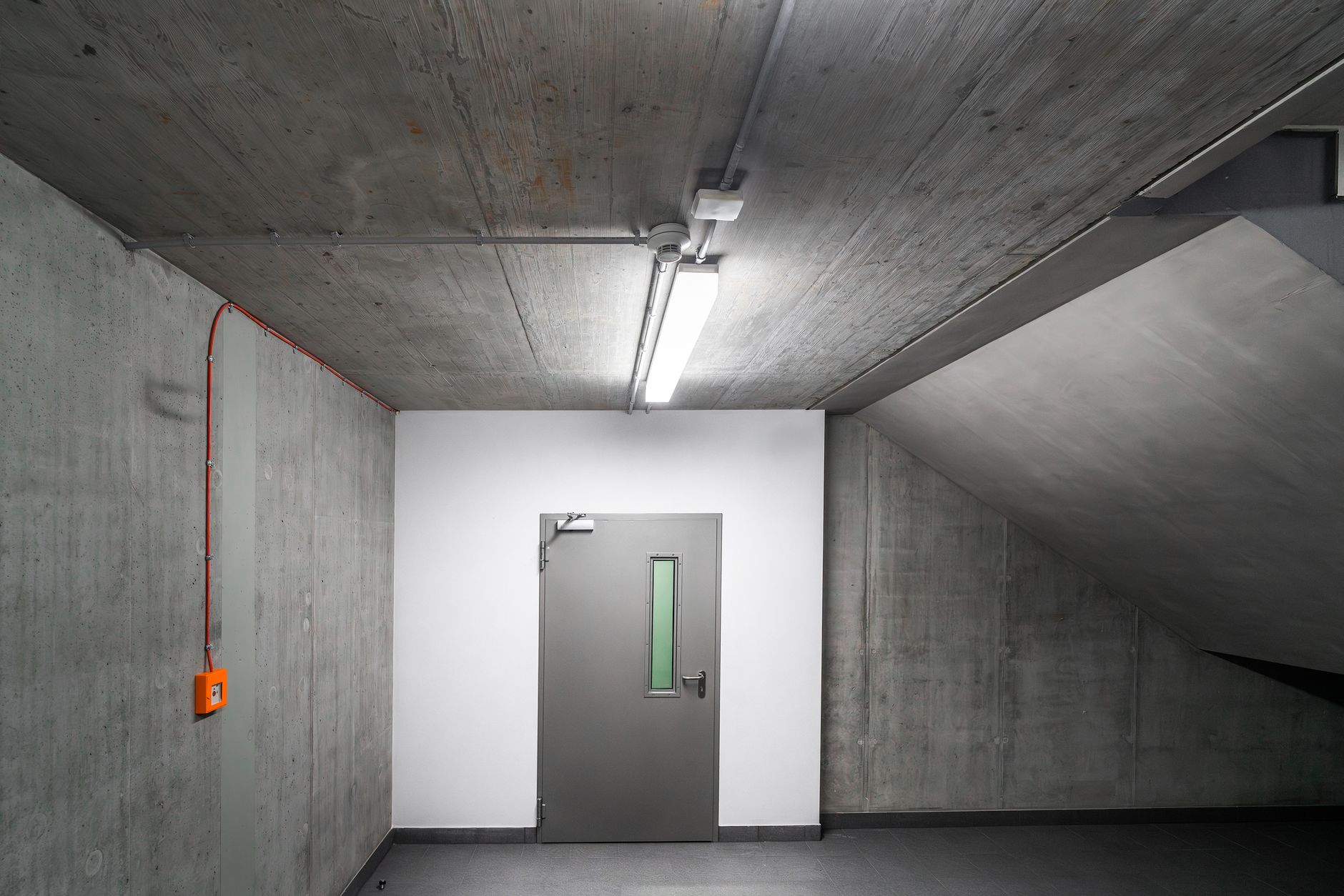 Stark and minimalist basement featuring a gray emergency door and industrial design.