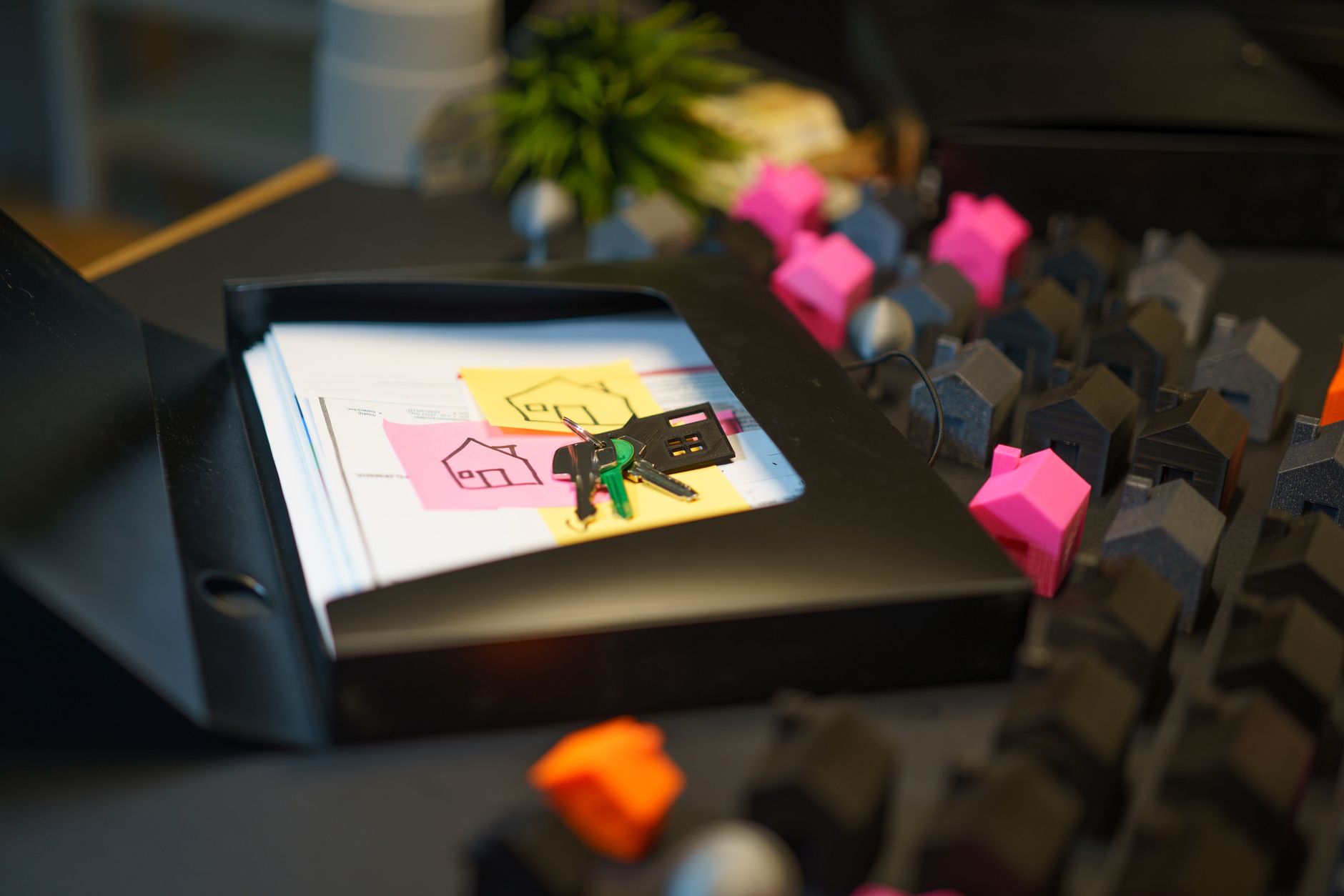 Keys and real estate documents on a desk surrounded by colorful house models, symbolizing property transactions.