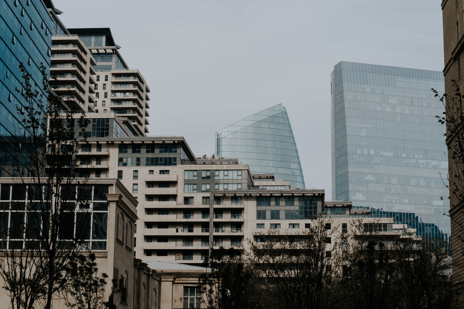 Urban skyline featuring contemporary high-rise buildings with glass facades against a cloudy sky.