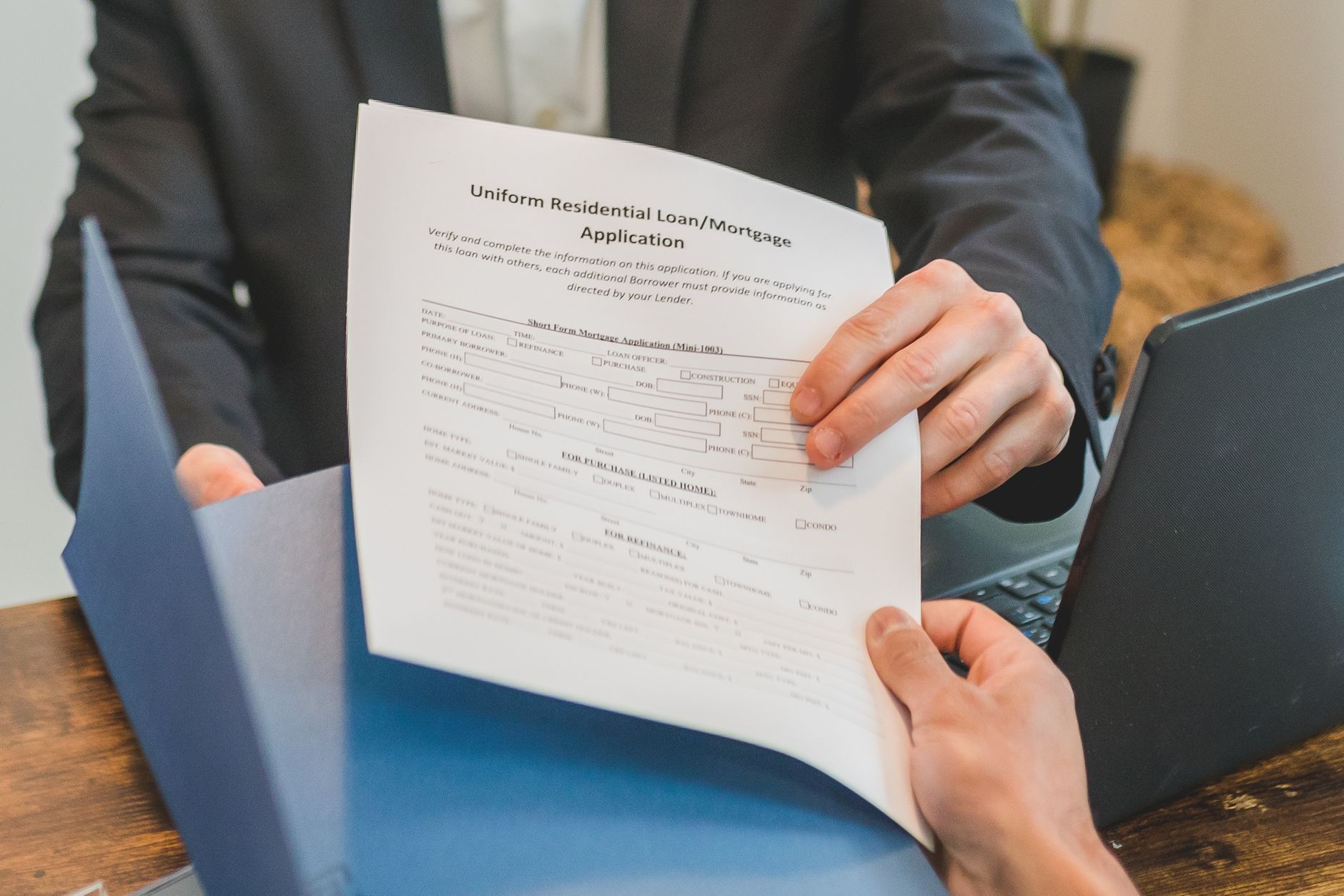 Professional setting showing hands exchanging a mortgage application document indoors.